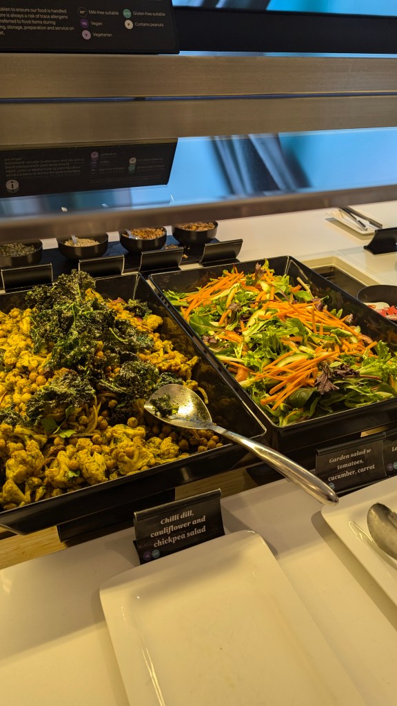 A buffet display featuring two salad dishes: a chilli dill cauliflower and chickpea salad alongside a garden salad with tomatoes, cucumber, and carrots.