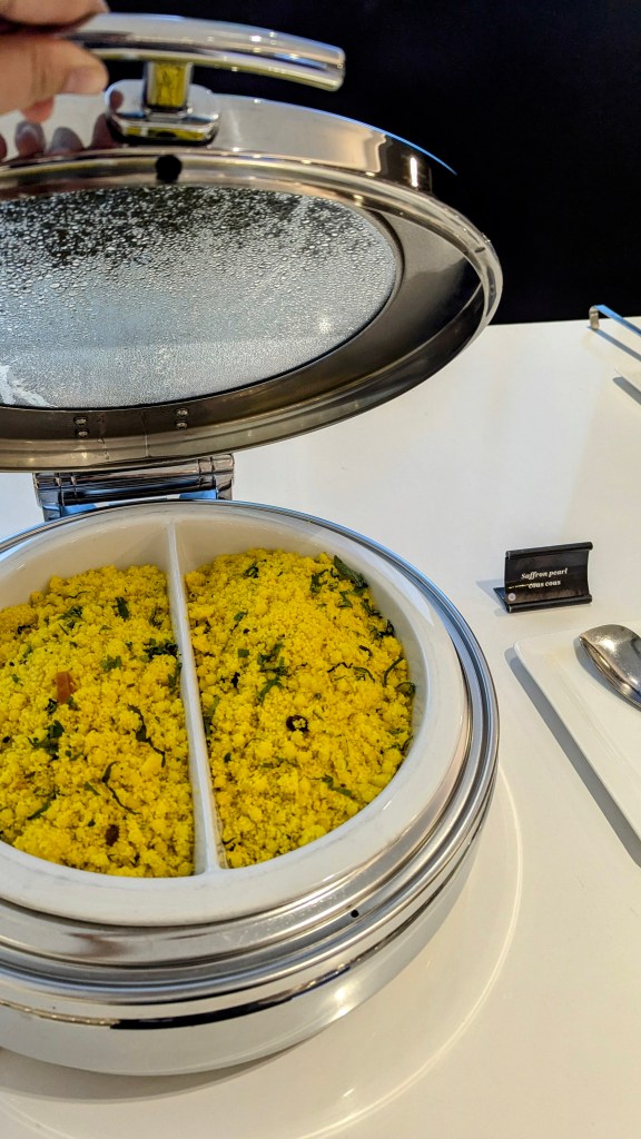 Close-up view of a dish containing saffron rice with garnishes in a stainless steel serving container, partially opened.
