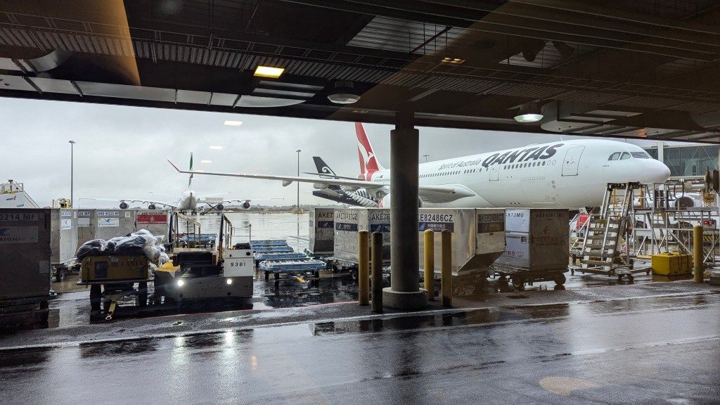 View of Qantas airplanes and airport service vehicles at a rainy airport terminal.