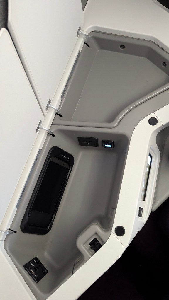 Interior close-up of the business class seat storage area on a Thai Airways Boeing 787-9, featuring charging ports and space for personal items.