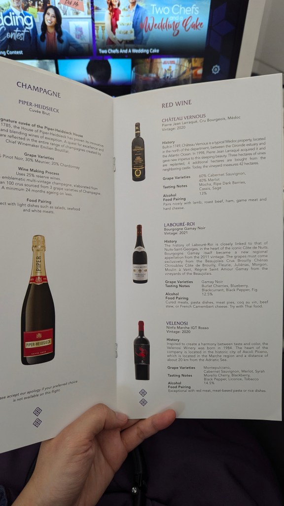 Wine menu featuring champagne and red wine options in Thai Airways business class with a background of in-flight entertainment.
