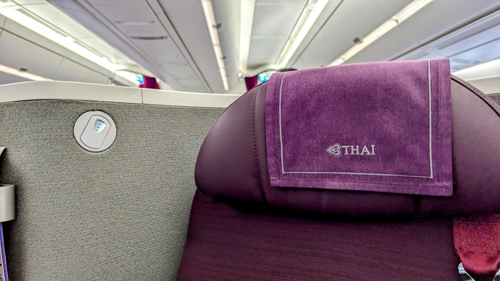 Close-up of the business class seat in a Thai Airways Boeing 787-9, featuring a purple headrest and power outlet beside the seat.